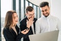 Cheerful company workers look into a laptop and laugh.