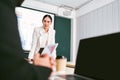 A cheerful and confident Asian businesswoman stands, present bar charts data from projector screen to her office colleagues. Royalty Free Stock Photo