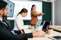A cheerful and confident Asian businesswoman stands, present bar charts data from projector screen to her office colleagues. Royalty Free Stock Photo