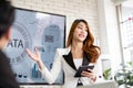 A cheerful and confident Asian businesswoman stands, present bar charts data from a whiteboard to her office colleagues. Royalty Free Stock Photo