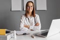 Cheerful confident female doctor working at office desk and smiling at camera wearing white lab coat and glasses posing with Royalty Free Stock Photo