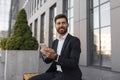 Cheerful confident young european male ceo manager with beard in suit chatting on phone, sits on bench