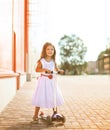 Cheerful cool little joyful girl in dress on the scooter