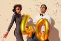 Cheerful couple celebrates a forty years birthday with big golden balloons and colorful little pieces of paper in the air