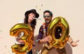 Cheerful couple celebrates a thirty years birthday with big golden balloons