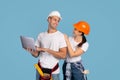 Cheerful couple in hardhats posing with laptop computer on blue studio background Royalty Free Stock Photo