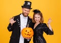 Cheerful couple in carnival costumes does scary gesture and celebrate Halloween on colored yellow background