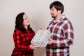 A couple in red checkered home clothes hands a gift packed with a bow of ribbon