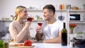 Cheerful couple with wine glasses spending time together at kitchen, romance