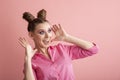 Cheerful crazy surprised girl with two bun hairstyles on a pink background. Adults are like children. Pink mood