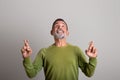 Cheerful curios old european man with beard shows fingers up on empty space on gray studio background