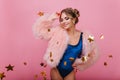 Cheerful curly girl in velvet bodysuit posing with eyes closed standing on pink background. Charming young woman fur Royalty Free Stock Photo