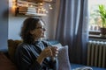 Cheerful curly young woman in warm sweater glasses enjoying a mug of tea while sitting on the sofa at home Royalty Free Stock Photo