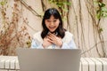 Cheerful asian girl making video call on laptop while sitting outdoors Royalty Free Stock Photo