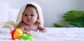 Cheerful baby lying on bed under white blanket looking at his color toy. Innocence baby crawling on white bed with his toy Royalty Free Stock Photo