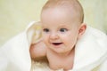 Cheerful cute baby under white blanket looking at something. Newborn child relaxing in bed after bath or shower. Childhood and Royalty Free Stock Photo