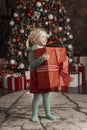 Cheerful cute child girl with gift. Little blonde girl holds big box with present, xmas tree background. Merry Christmas Royalty Free Stock Photo