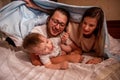 Cheerful family hiding with baby son under blanket. Mother and father try to catch an active baby Royalty Free Stock Photo