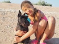 A cheerful cute girl is sitting and hugging her dog on the beach. Cute blonde girl with her dog on the sea, the concept of love Royalty Free Stock Photo