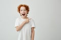 Cheerful cute little boy with curly ginger hair and freckles happy smiling and pointing aside with finger on white Royalty Free Stock Photo