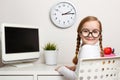 Cheerful cute little girl a schoolgirl with glasses sits at a table. The child on the background of the student workplace Royalty Free Stock Photo