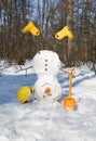 Cheerful cute snowman in yellow boots with a shovel and a construction helmet turned upside down in a snowy forest Royalty Free Stock Photo