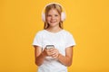 Cheerful cute teen blonde girl in headphones use phone and looks at camera Royalty Free Stock Photo