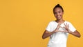 Cheerful cute teenage afro american girl in white t-shirt showing heart sign on chest