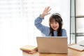 A cheerful and cute young Asian girl is raising her hand to answer a question while studying online