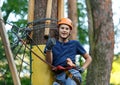 Cheerful cute young boy in blue t shirt and orange helmet in adventure rope park at sunny summer day. Active lifestyle, sport, Royalty Free Stock Photo