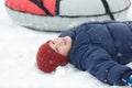 Cheerful cute young boy in orange hat and blue jacket holds tube on snow, has fun, smiles. Teenager on sledding Royalty Free Stock Photo