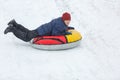 Cheerful cute young boy in orange hat and blue jacket holds tube on snow, has fun, smiles. Teenager on sledding Royalty Free Stock Photo