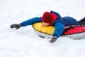 Cheerful cute young boy in orange hat red scarf and blue jacket holds tube on snow, has fun, smiles. Teenager on sledding Royalty Free Stock Photo