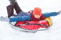 Cheerful cute young boy in orange hat red scarf and blue jacket holds tube on snow, has fun, smiles. Teenager on sledding Royalty Free Stock Photo