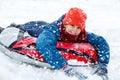 Cheerful cute young boy in orange hat red scarf and blue jacket holds tube on snow, has fun, smiles. Teenager on sledding Royalty Free Stock Photo