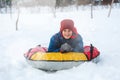 Cheerful cute young boy in orange hat red scarf and blue jacket holds tube on snow, has fun, smiles. Teenager on sledding Royalty Free Stock Photo