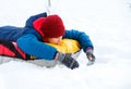 Cheerful cute young boy in orange hat red scarf and blue jacket holds tube on snow, has fun, smiles. Teenager on sledding Royalty Free Stock Photo