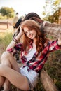 Cheerful cute young woman cowgirl siting on farm