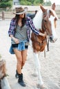 Cheerful cute young woman cowgirl walking with her horse Royalty Free Stock Photo