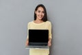 Cheerful cute young woman standing and holding blank screen laptop Royalty Free Stock Photo