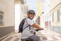 Cheerful cyclist elderly woman in urban street carrying a backpack, wearing helmet running with electro bicycle. Concept of