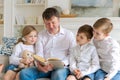 Cheerful dad with children are sitting on couch and reading book, preschoolers Royalty Free Stock Photo