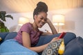 Cheerful darkskinned young woman with smartphone on sofa
