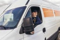 Cheerful delivery driver looking out the window of the white cargo van vehicle, delivering goods by car Royalty Free Stock Photo