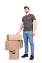 Cheerful delivery man wearing cap, full length portrait, stands near cardboard parcel boxes, isolated on white background. Happy Royalty Free Stock Photo