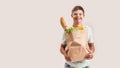 Cheerful disabled boy with Down syndrome smiling at camera while holding paper bag with food, standing isolated over Royalty Free Stock Photo