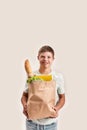 Cheerful disabled boy with Down syndrome smiling at camera while holding paper bag with food, standing isolated over Royalty Free Stock Photo