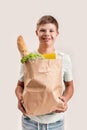 Cheerful disabled boy with Down syndrome smiling at camera while holding paper bag with food, standing isolated over Royalty Free Stock Photo