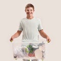 Cheerful disabled boy with Down syndrome smiling at camera while holding a recycling bin full of paper waste, standing Royalty Free Stock Photo