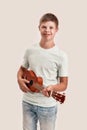 Cheerful disabled boy with Down syndrome smiling at camera while playing ukulele, standing isolated over white Royalty Free Stock Photo